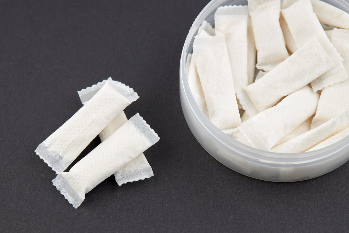 Open tin of white functional pouches with loose pouches beside it