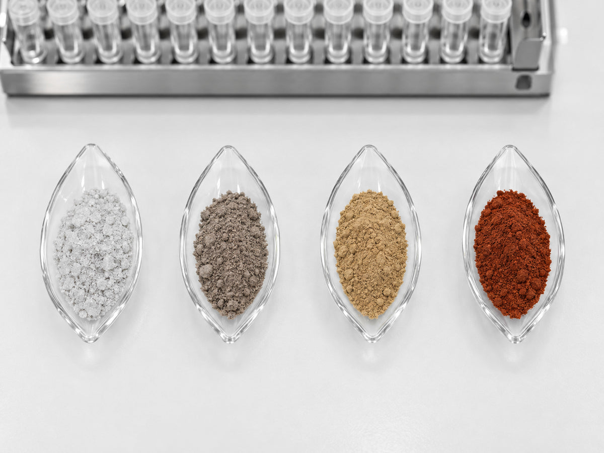 Four iron powders in glass weighing boats, from greyish white to rust red, beside an ICP-MS rack